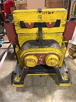 Front view of the large yellow wood mold with face-like design, showing eyes painted black and red, large circular nose shapes, and thick supportive legs.