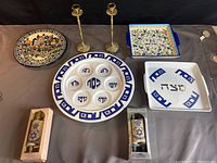 Full lot view showing all items: Passover Seder plate, Jerusalem decorative plate, two serving plates, two candlesticks, and two miniature Torah scrolls.