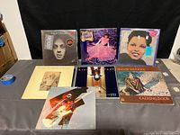 Seven classic rock and soul vinyl albums displayed on a table showing full cover artwork, including Billy Joel, Stevie Wonder, and others.