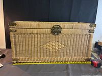 Full front view of rectangular wicker chest with ornate metal latch and corner pieces featuring bird designs.