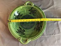 Top view showing the full circular green ceramic platter with black sea turtle designs and measuring tape indicating approximately 14 inches in diameter.