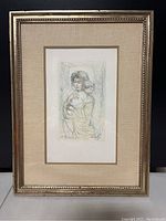 Framed lithograph of a woman holding a child, showing full piece with linen matting and gold frame.