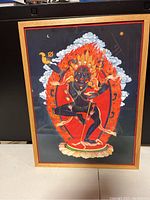 Frontal shot of Tibetan Buddhist deity framed artwork showing full figure in vibrant colors with wood frame and glass protection