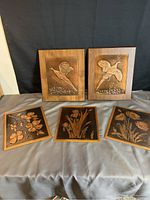 Complete view of five copper wall art pieces; two bird scenes framed in wood and three flower scenes framed in copper, arranged and laid out
