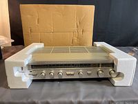 Front view of silver Technics SA-203 stereo receiver inside white foam packaging with cardboard box behind