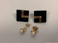 Wide view showing both pairs of stud earrings, one with black onyx and gold V shape, the other with small cultured pearls and gold prongs.