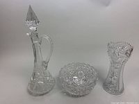 Photo of three vintage cut crystal pieces: lidded decanter, round bowl, and tall vase showing clear detailed cut patterns.