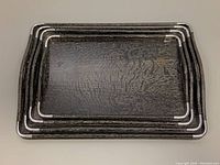 Top view of four nesting serving trays stacked inside one another showing dark wood grain texture and metal corner braces