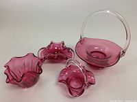Four cranberry glassware pieces on white background including three baskets and one ribbed ashtray, all in cranberry glass with some clear accents.