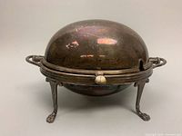 Front and top angled view of antique silver plate domed roll top warming chafing serving dish on claw feet with side handles, showing overall condition and tarnish.