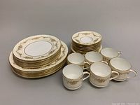 Full set showing stacked dinner plates, luncheon plates, dessert plates, mugs, and saucers with gold decorative accents.