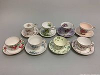 Overview of all eight bone china teacup and saucer sets arranged in two rows, each with unique floral designs and gold trim.