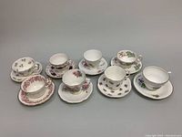 Eight bone china teacup and saucer sets arranged in two rows showing various floral and decorative patterns on white background.