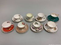 Eight bone china Aynsley teacup and saucer sets arranged on a plain surface, displaying a variety of colorful and floral patterns with gold detailing.