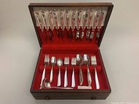 Full view of flatware set in wooden chest showing all items inside, with red interior lining and lids open.