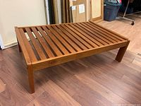 Full view of the rectangular wooden coffee table with horizontal slatted top and four square legs on wood floor.
