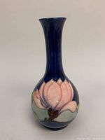 Front view of cobalt blue porcelain bud vase with raised pink flower decoration.