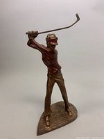 Front-left angled view of the vintage woman golfer sculpture showing golfer's facial features, visor, upper body, and club position.