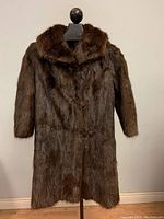 Full view of the vintage muskrat fur coat hanging on a mannequin showing length and overall condition.