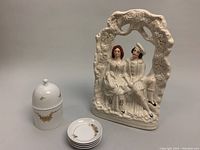 Lidded porcelain jar and four condiment dishes arranged next to ceramic sculpture showing relative sizes and overall lot contents.
