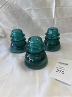 Three blue Hemingray glass insulators displayed on a white cloth background.