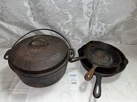 Photo of the entire lot showing Wagner Ware drop roaster with lid and two cast iron skillets next to it on a white fabric background.