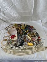 Pile of mixed costume jewelry including necklaces, bracelets, brooches, rings, and earrings displayed on white cloth