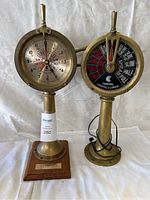 Full view of two brass maritime instruments, a clock and an engine order telegraph, standing side by side on white fabric.