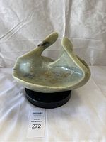 Front view of light green jade abstract sculpture showing shape and color with natural veining and cracks, placed on black stand.
