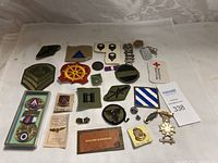Photo showing an assortment of military patches, pins, medals, and dog tags spread on a white cloth.