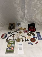 Wide view of all military patches, pins, coins, and accessories spread out on white fabric background with seller card