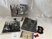 Vintage black and white photographs of men, embroidered patches and printed historical card displayed on white cloth