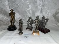 Five metal figurines representing Napoleon Bonaparte and historical soldiers along with bases shown on a white fabric background.