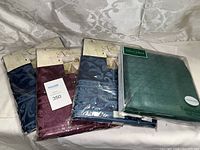 Four packaged table cloths folded, three from Richelieu in navy and burgundy colors, one Villeroy & Boch green cloth.