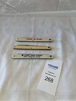 Three vintage sausage cutters in folded position, showing handles with brand names and logos.