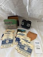 Full layout of vintage View-Master viewer, box, 16 reels, and original papers on white cloth background