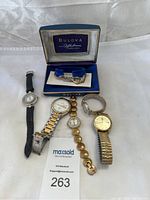 Photo of six wristwatches arranged on a white background including Bulova watch in box and several metal and leather band watches