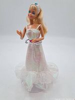 Front view of 1990's vintage Barbie doll standing in iridescent white gown with ruffled tulle hem and pink belt. Doll has long blonde hair.