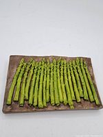 Front view of rectangular ceramic wall art showing green asparagus spears on brown textured base.