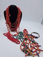 Photo showing full assortment of beaded necklaces and bracelets on white background with black bust