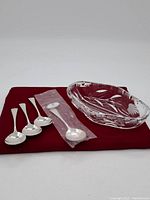 Four silverplated spoons and one sealed spoon beside a clear crystal bowl on a red cloth.