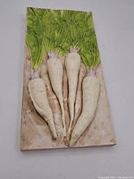 Full front view of rectangular relief wall art depicting four white carrots with green leafy tops on a beige background.