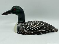 Side view of the carved and painted wooden loon decoy showing smooth lines, detailed paint spots, and red eye.