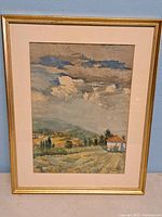 Full frontal photo of framed watercolour painting showing rural European landscape with fields, trees, hills, small house, and cloudy sky.