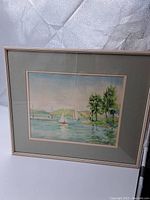 Framed watercolor painting showing a sailing scene with multiple sailboats, green trees, and hills under blue sky.
