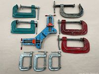 Top-down view of one blue joint-angle clamp surrounded by eight assorted C-clamps in green, red, and silver finishes.