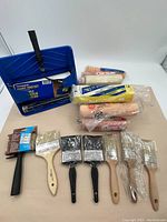 Blue paint pad set with roller frame on top left, several paint rollers and multiple paintbrushes below and to the right.