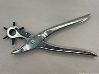 Full view of the metal leather hole punch tool showing the handle and rotating punch head with six punch sizes.