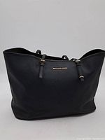 Front view of black Michael Kors handbag with gold logo and straps