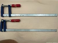 Pair of 24-inch wood clamps laid flat on a beige surface showing blue clamp arms, metal bars, and red handles.